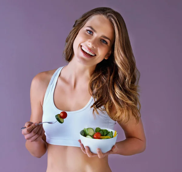 健康的な食事はあなたの体と心のために素晴らしいです 健康的な若い女性のスタジオショット笑顔と紫色の背景にサラダとポーズ — ストック写真