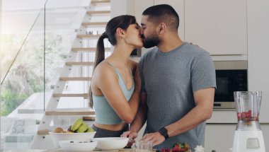 Aşk, yemek pişirme ve mutfakta öpüşen çiftler sağlıklı, taze ve diyet bir kahvaltı hazırlarken. Mutlu, kaynaşmış genç bir adam ve kadın, meyve suyu için birlikte meyve keserken....