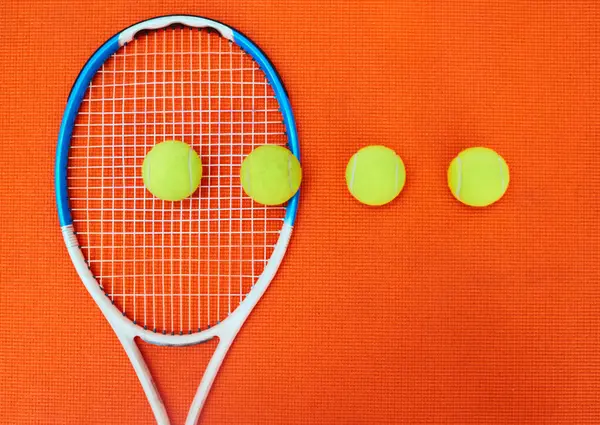 すべてが列に並んでいた スタジオ内のオレンジの背景に置かれた1つのテニスラケットといくつかのテニスボールの高角度ショット — ストック写真