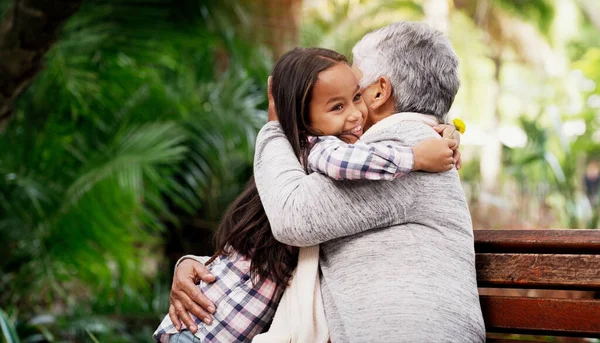 stock image Happy, young girl and grandmother hug or a flower for senior woman or child with care or bond with pensioner and summer day in the park. Joy, kid and elderly person embrace on the bench with love.