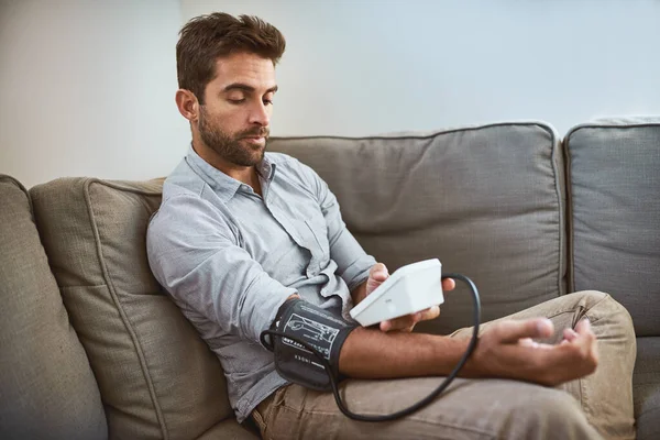 自宅のソファや医療や健康テストのためのリビングルームで高血圧 機械と男の試験血圧 ストレスによる慢性疾患のための機器の監視 読書や人 — ストック写真