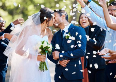 Yeni evli çift gelin ve damat, arkadaşları ve aileleriyle öpüşürken düğün töreninden sonra konfeti gül yapraklarıyla yıkanırlar..