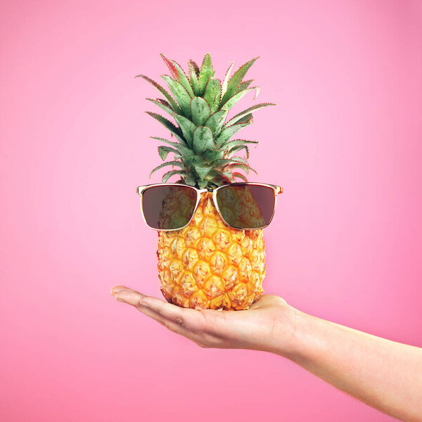 Cooler than a pineapple. a woman holding a pineapple with sunglasses on