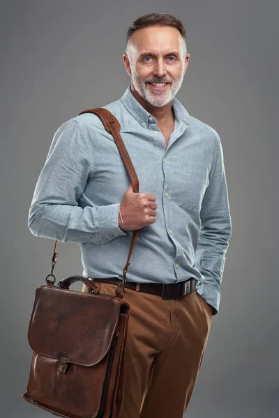 スタイルで事務所に向かう グレーの背景にバッグを持った大人の男のスタジオポートレート — ストック写真