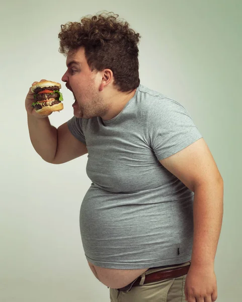 ちょっと幅を広げて スタジオショットの太りすぎの男のハンバーガーにかむ — ストック写真