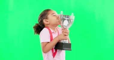 Yeşil ekran stüdyo arka planında izole edilmiş kupasıyla mutlu, kazanan ve yüzü olan bir çocuk. Heyecanlı, başarılı ve bir kızın portresi spor, başarı ve maket ile bir ödülü öpüyor..