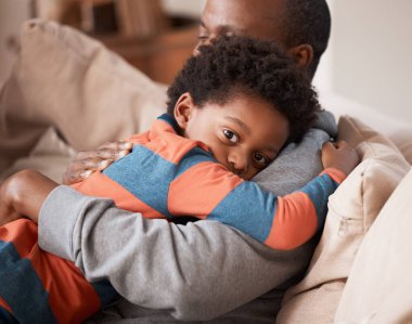 Aşk, portre ve evlerinin oturma odasındaki kanepede dinlenirken babasına sarılan çocuk. Bakım, güvenlik ve korkmuş Afrikalı çocuk, aile evinde rahatlık veya bağ kurmak için babasını kucaklıyor..