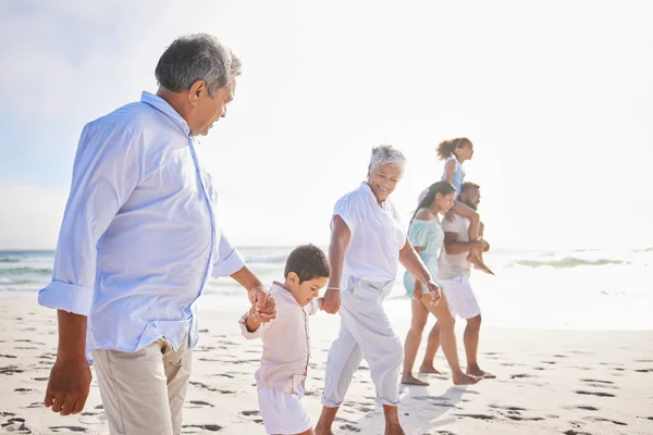Big family, vacation and holding hands walking on beach for fun bonding, holiday or weekend together in nature. Grandparents, parents and children on ocean walk by the coast on mockup space outdoors.