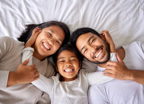Love, selfie and family in bed from above happy, smile and bonding in their home together. Portrait, girl child and top view of parents with their daughter in a bedroom, relax and embracing indoors.