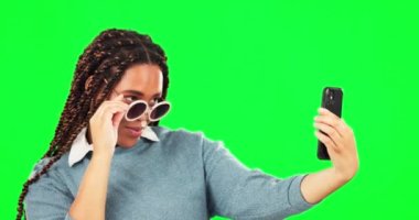 Stüdyoda profil fotoğrafı için yeşil ekranlı bir kadınla selfie, güneş gözlüğü ve tavır. Sosyal medya durumu güncellemesi için poz veren havalı bir kadınla fotoğraf, moda ve tarz..