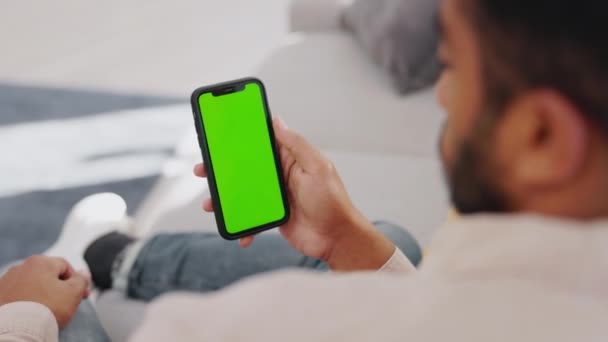 ソファーで男 携帯電話の画面と緑のモックアップは ソーシャルメディア オンラインユーザーや視聴サブスクリプションにリラックスする スマートフォンやモバイルアプリ上のブランクモックアップ ゲームをダウンロードし デジタル接続 — ストック動画