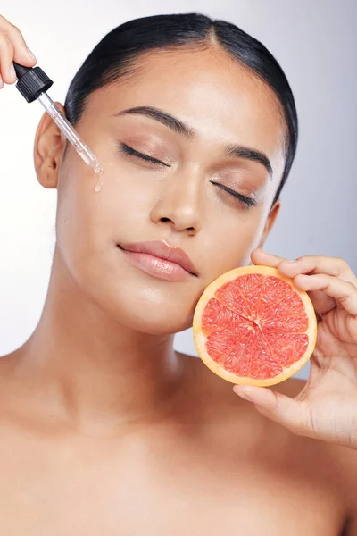 Woman, face and serum with beauty and grapefruit, skincare oil with natural cosmetics isolated on studio background. Fruit, female model with pipette and vitamin c acid for skin with dermatology.