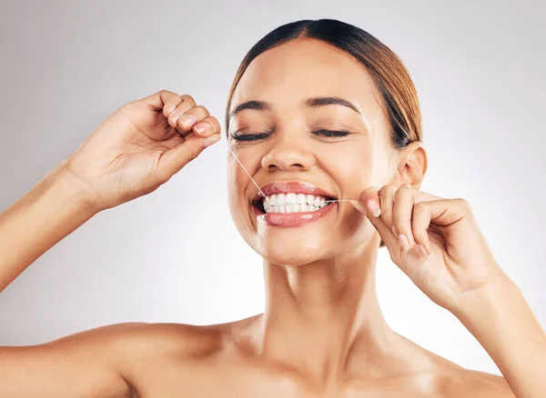 Stock image Smile, oral care and woman flossing teeth in studio for hygiene, wellness or fresh breath on grey background. Face, floss and lady relax with mouth, tooth or cleaning for dental or cavity prevention.