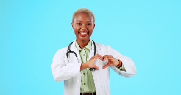 青い背景のスタジオで心の形の手や笑顔で幸せな黒人女性 肖像画や医師 愛のシンボルやサインで笑顔医療やウェルネスを持つモックアップスペースやアフリカの看護師 — ストック動画