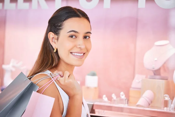 Jewelry store, window and a woman with a shopping bag in mall for fashion, sale or discount deal. Female person or customer portrait with a smile at retail shop with diamonds, jewellery and promotion.