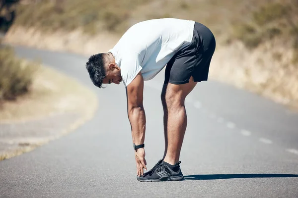 Stretching, running and fitness with man in road for training, workout and exercise. Muscle, energy and cardio performance with male runner and warm up in nature for marathon, start and health.