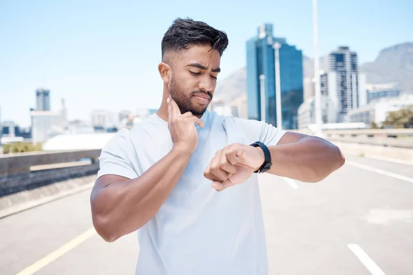 Fitness, man and watch in city for pulse, heart rate or checking performance after workout or exercise. Fit, active and sporty male person, athlete or runner looking at wristwatch for cardio health.
