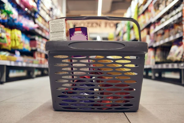 Closeup of basket with groceries, floor with shopping and supermarket, food product with retail and stock. Grocery choice, store shelf and aisle with merchandise, commercial service with shop sale.