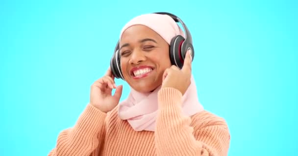 幸せな女性 ヘッドフォンやダンスの青の背景のお祝いや歌のための音楽を聞いて孤立した スタジオでストリーミング技術を持つ面白い ダンスやイスラム教徒 ジェンZやヒジャーブ人 — ストック動画