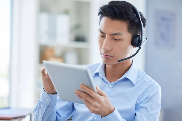 Call center, tablet and focus with asian man in office for consulting, customer service and contact us. Communication, focus and help desk with male employee for technology, digital and networking.