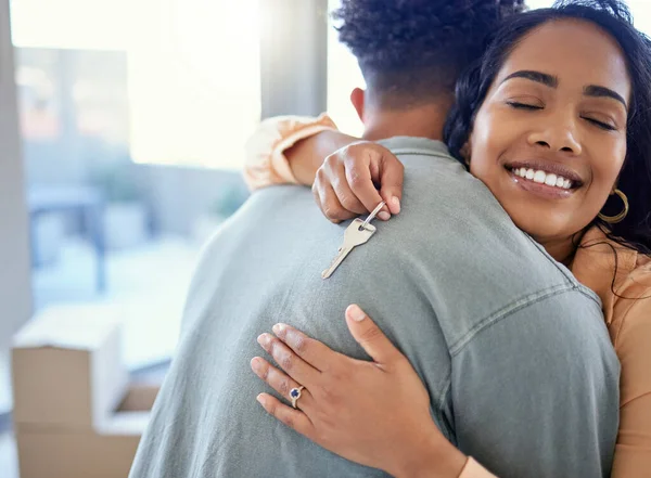 Happy couple, hug and real estate with key for moving in new home or mortgage loan together indoors. Woman hugging man with smile in happiness, property or investment with keys to apartment building.