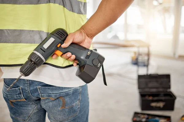 Construction, handyman and drill in hand of a man for maintenance or carpenter work. Back of male engineer, constructor or contractor worker with electric power tools at building site for renovation.