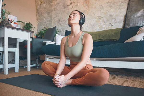 Focus on developing a connection between the body and the breath. a young woman wearing headphones while exercising at home