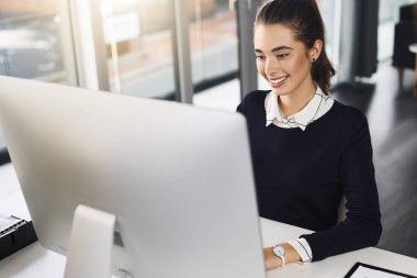 İşim beni mutlu ediyor. Çekici genç bir iş kadını masasında oturuyor ve bilgisayarını modern bir ofiste kullanırken gülümsüyor.