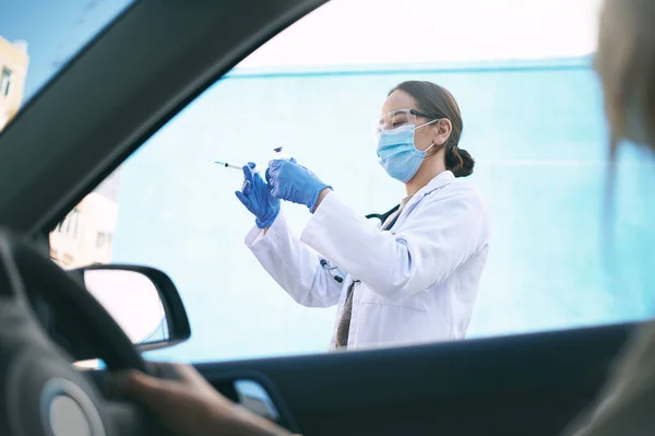 stock image The time to take action is now. a masked young doctor giving a patient an injection at a Covid-19 drive through testing centre