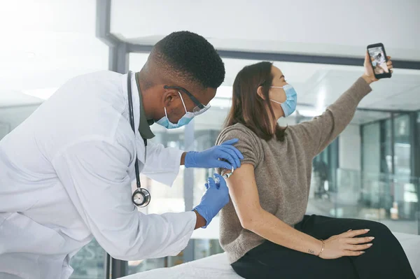 stock image Mandatory vaccine selfie. a young doctor giving a patient an injection while she takes a selfie in an office