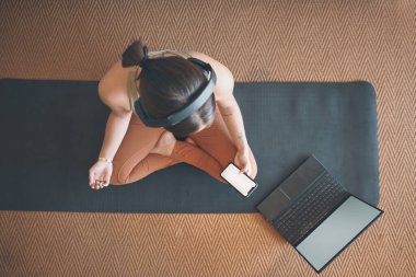 İnternetteki yoga uzmanlarından öğreniyorum. Genç bir kadının evde egzersiz yaparken cep telefonu ve dizüstü bilgisayar kullanırken yüksek açılı görüntüsü.