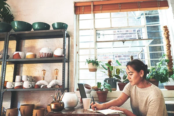 stock image I wouldnt be here today if it wasnt for notes. an attractive young business owner sitting alone in her pottery studio and making notes