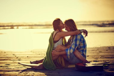 Aşk bir okyanus gibidir, derin ve sürekli hareket halindedir. Bir çift sahilde oturuyor, bacakları birbirine dolanmış.