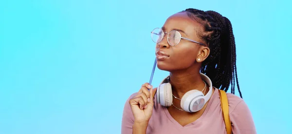 Black woman, thinking and gen z person with student vision and ideas in a studio copy space. Blue background, university students idea and headphones of a young female with glasses contemplating with.