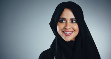 Gülümsemesini görmemek çok zor. Genç Müslüman bir iş kadınının gri bir arka planda çekilmiş bir fotoğrafı.
