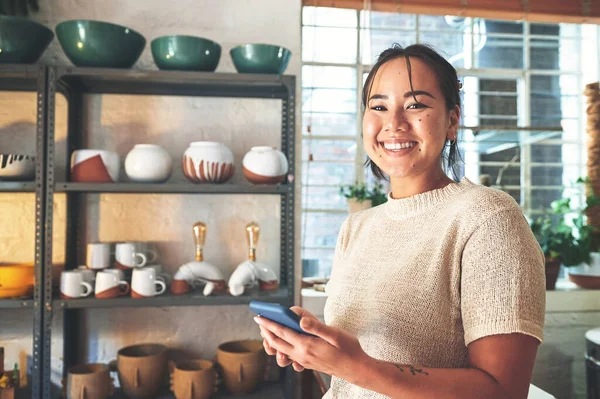 Stock image Youre welcome to send me a message. Cropped portrait of an attractive young business owner standing alone in her pottery studio and using her cellphone