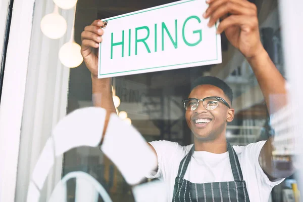 A growing business needs a growing team. a young man hanging up a hiring sign while working in a cafe