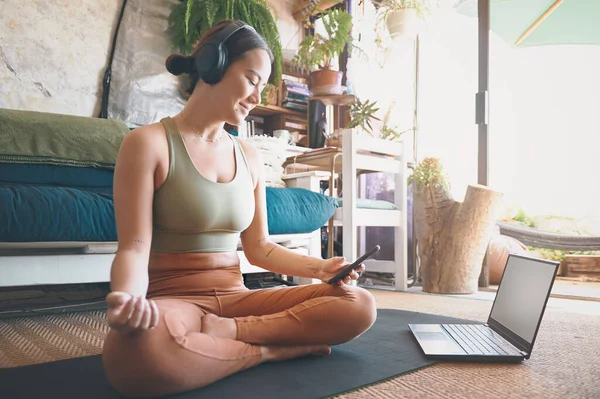 在科技的帮助下 你可以在家里练习瑜伽 在家里锻炼时使用手机和笔记本电脑的年轻妇女 — 图库照片