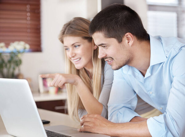 Finding out whats available on the world wide web. A couple standing in their kitchen looking on a laptop and smiling