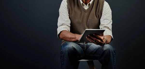 stock image Updating his lifestyle. Studio shot of an unrecognizable man using a tablet while sitting on a wooden stool against a dark background