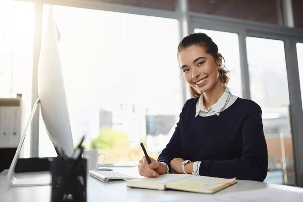 幸せな職場環境で 現代的なオフィスでメモを書きながら彼女の机に笑顔と座って魅力的な若いビジネスマンの肖像画 — ストック写真