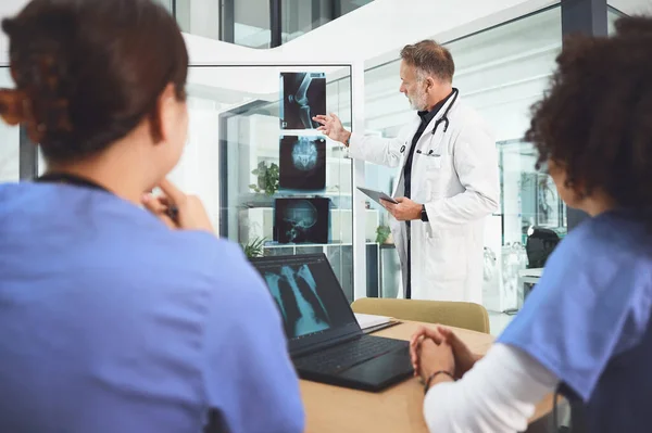 stock image Giving his team a clear guide to their tasks and responsibilities. a mature doctor analysing x-rays with his colleagues during a meeting in a hospital