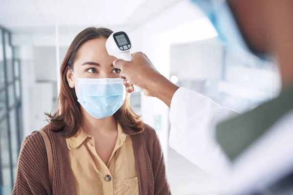 コヴィドにならないで マスクをした若い女性が診療所の先生に体温をチェックされ — ストック写真