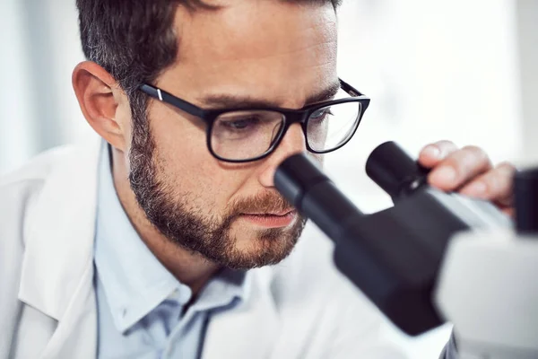 stock image It says interesting every time I do this. a focused young male scientist looking through a microscope while being seated inside of a laboratory