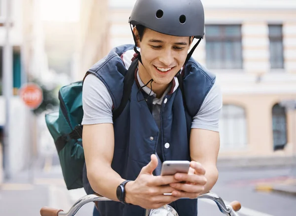 stock image Man, courier bicycle and smile with phone, order or e commerce app for food, product and sustainable transport. Young guy, bike and metro street with texting, chat and eco friendly with logistics job.