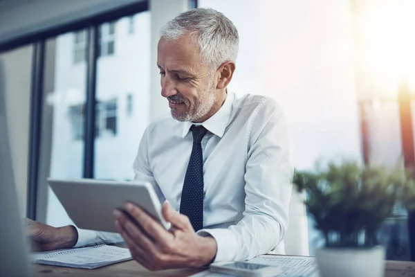 stock image Hes a tech savvy executive. a businessman sitting at his desk using a digital tablet