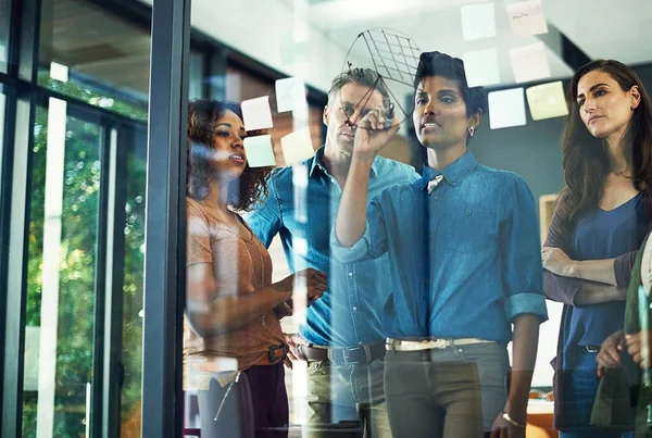 チームワークは企業を強化するものです オフィスのガラスの壁にメモでブレインストーミングしているビジネスマンのグループは — ストック写真