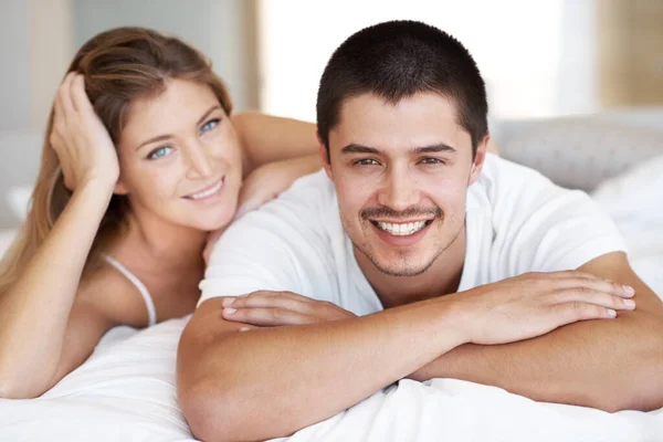 一緒にリラックスした品質の時間を過ごす 魅力的な若いカップルベッドに横たわっ一緒に広い笑顔 — ストック写真