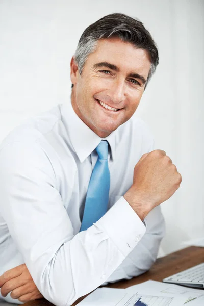 彼は企業の買収者だ 彼の机に笑顔で座っているハンサムな成熟したビジネスマン — ストック写真
