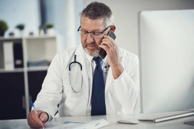 Kişisel olarak bir hastaya geri bildirim iletiyorum. Ofisindeki bir masada cep telefonu kullanan olgun bir doktor.